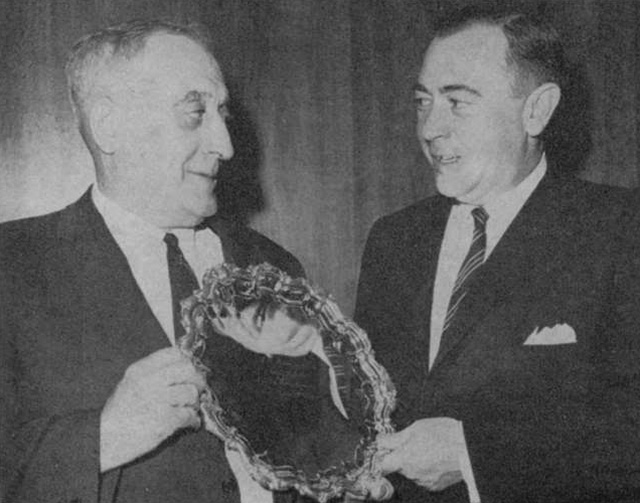 Two men in suits holding a plate trophy