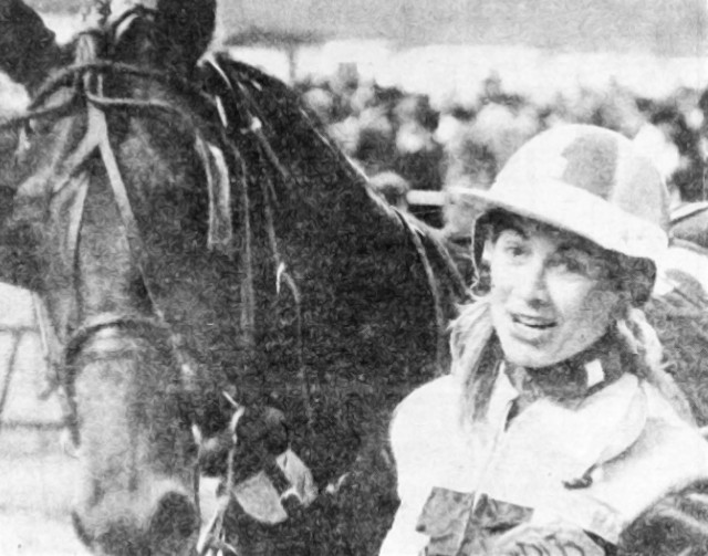 A woman in a racing suit holding a horse's head