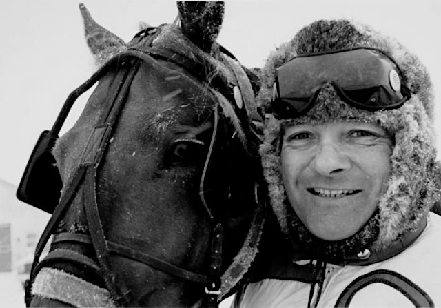 A man in a winter hat holding a horse's head