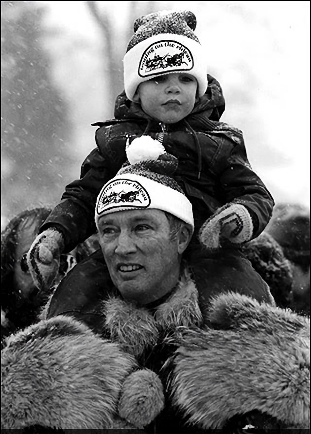 A man in winter clothes carries a child on his shoulders
