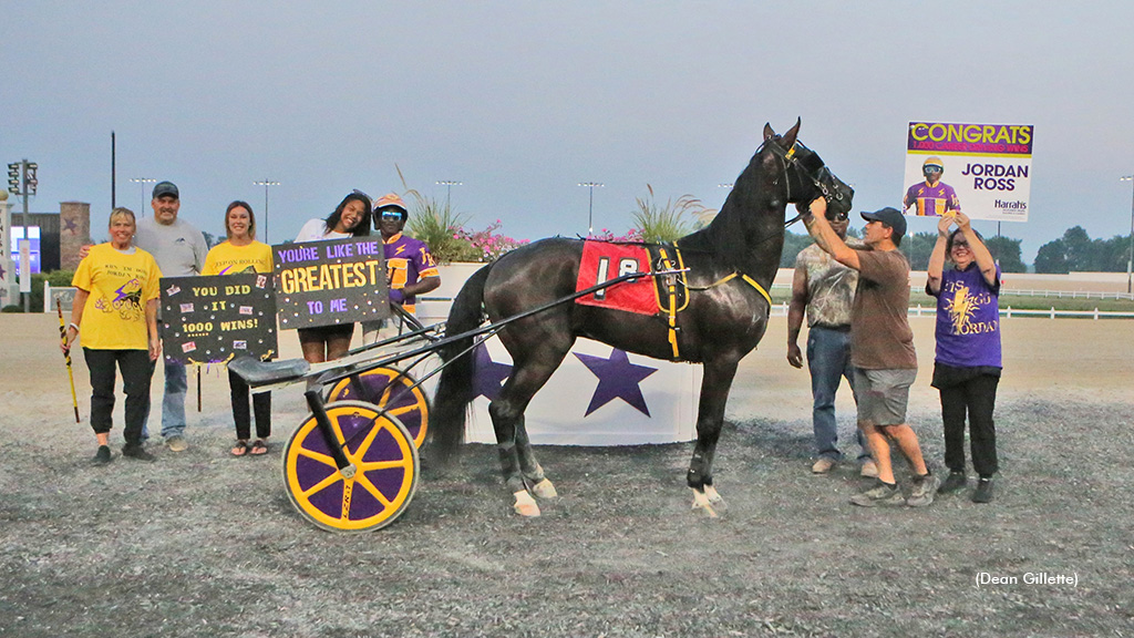 Jordan Ross in the winner's circle behind his horse with friends and family holding celebratory signs.