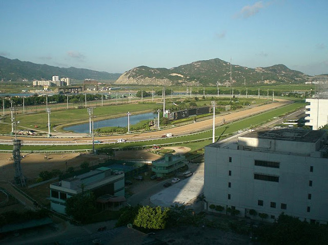 The Macau Jockey Club racecourse, showing the racetrack with a turf and dirt course with mountains the background.