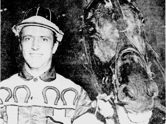 A man in racing colours holds a horse's head