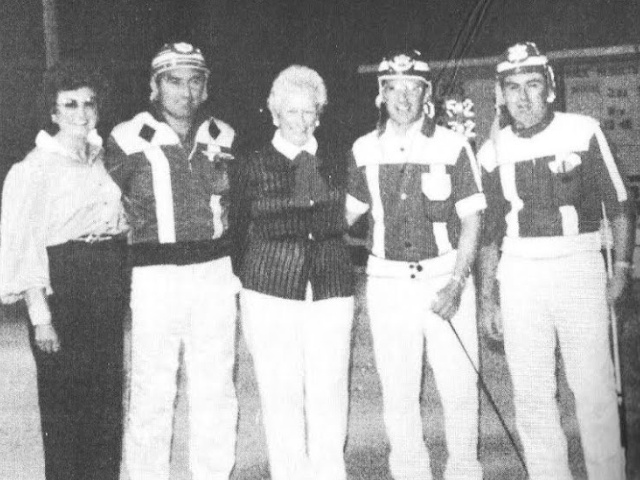 Three drivers in racing colours stand with two women
