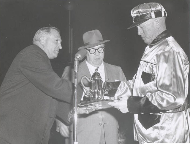 A driver in racing colorus receives a trophy