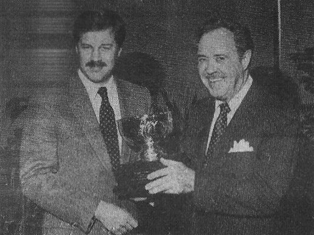 Two men in suits holding a trophy