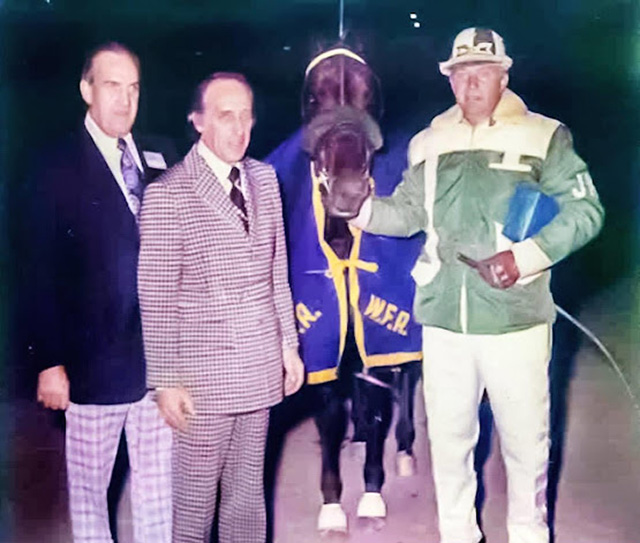 Two men in suits, next to a man in driving colours holding a horse