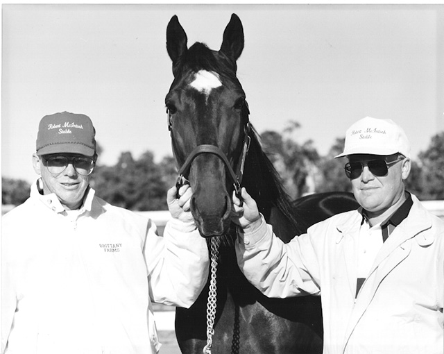 Two men in caps hold a horse