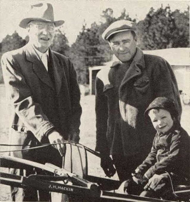 Two men stand behind a young boy in a sulky