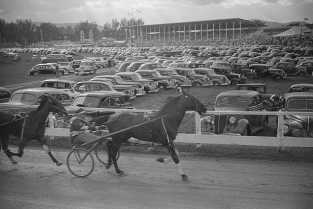 Horses racing around a track with old-style cars in the infield