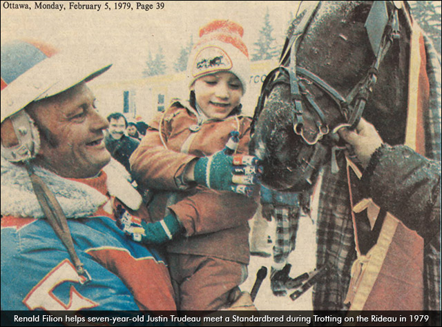 A man holding a child up to pet a horse's nose