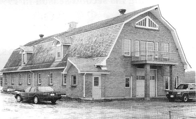 A barn with a tiled roof and a balcony with two cars parked in front