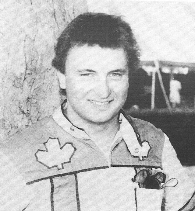 A man in racing colours in front of a tree