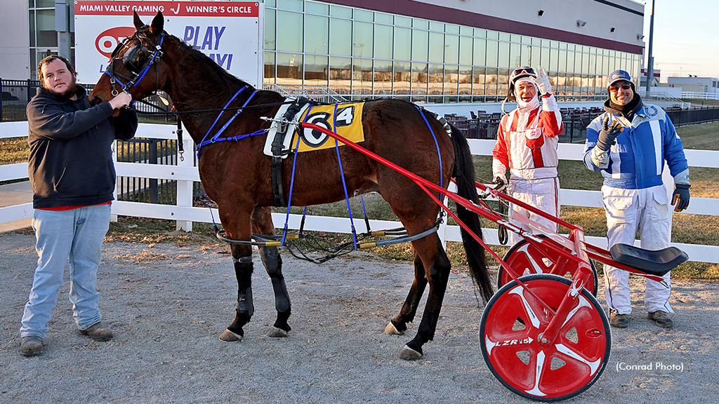 Jeremy Smith holds up four fingers in the winner's circle next to the winning horse and trainer